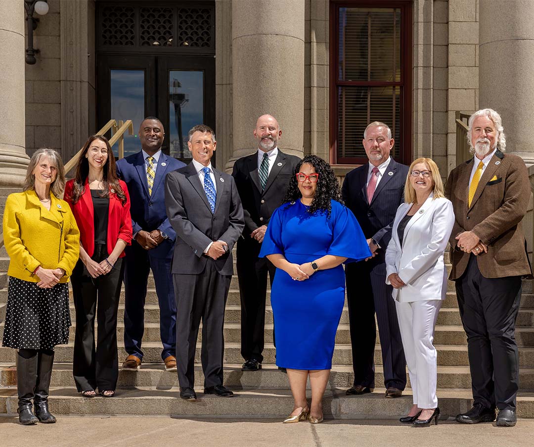 A group photograph of Colorado Springs Utilities Board members on the steps of city hall. Members pictured from left to right are Nancy Henjum, Brandy Williams, Roland Rainey, Brian Risley, Dave Donelson, Kimberly Gold, Tom Bailey, Lynette Crow-Iverson and David Leinweber.