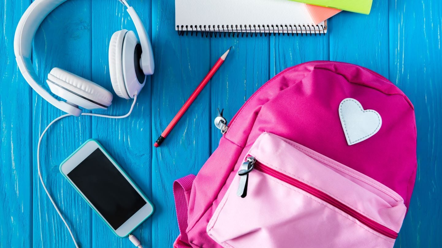 A photo of a pink backpack, a smartphone, pencil and notebook on a table.